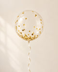 Clear bubble balloon filled with gold round confetti and finished with an ribbon