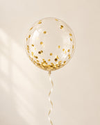 Clear bubble balloon filled with gold round confetti and finished with an ribbon