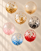 Seven clear bubble balloons with gold, blush pink, baby blue, and black confetti, red confetti, gold sparkle, and gold-and-ivory mini balloons, finished with ivory ribbons.

