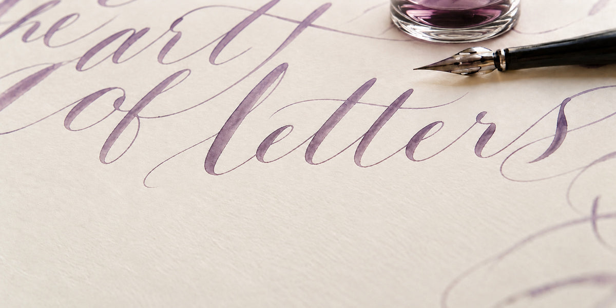 Close-up of calligraphy on cream paper beside a black dip pen and glass inkwell
