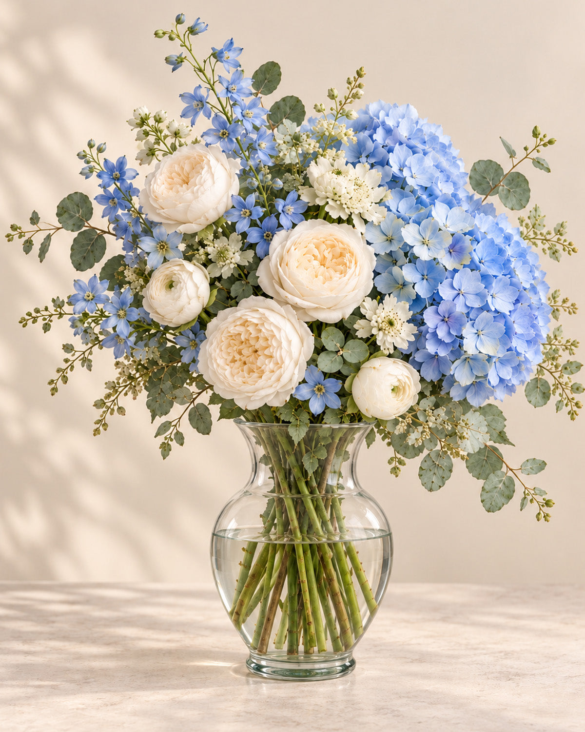 Blue Cloud bouquet with blue hydrangea, white peonies, blue delphinium, and eucalyptus arranged in a vase