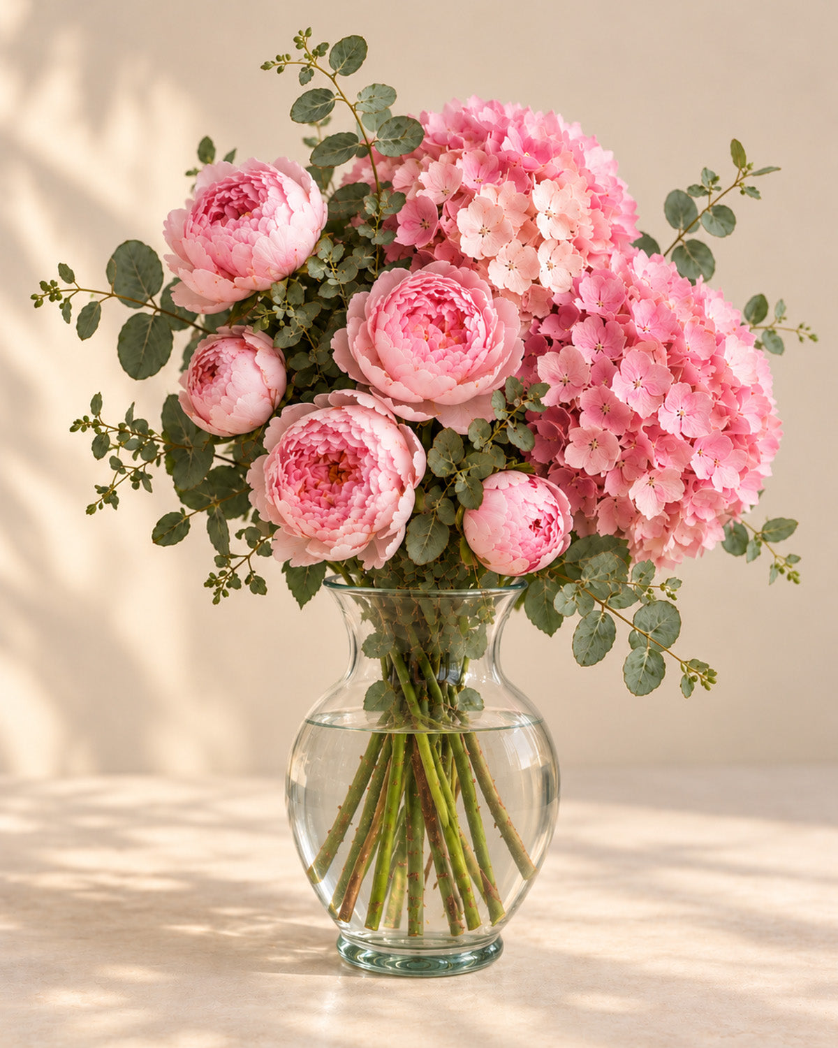 Pink Cloud bouquet with pink peonies, hydrangea, and eucalyptus arranged in a clear glass vase