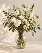 White Linen bouquet with white roses, lisianthus, snapdragons, delicate white flowers and greenery in a clear glass vase