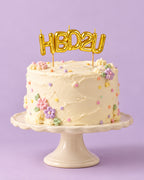 Gold "HBD2U" letter candles on a frosted birthday cake