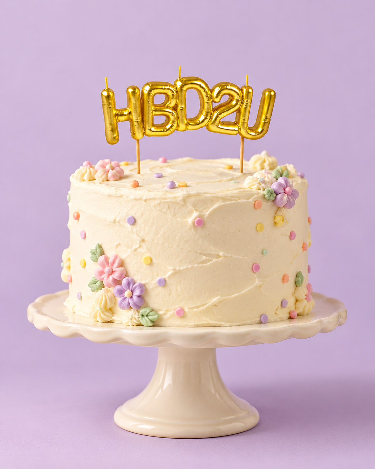 Gold "HBD2U" letter candles on a frosted birthday cake