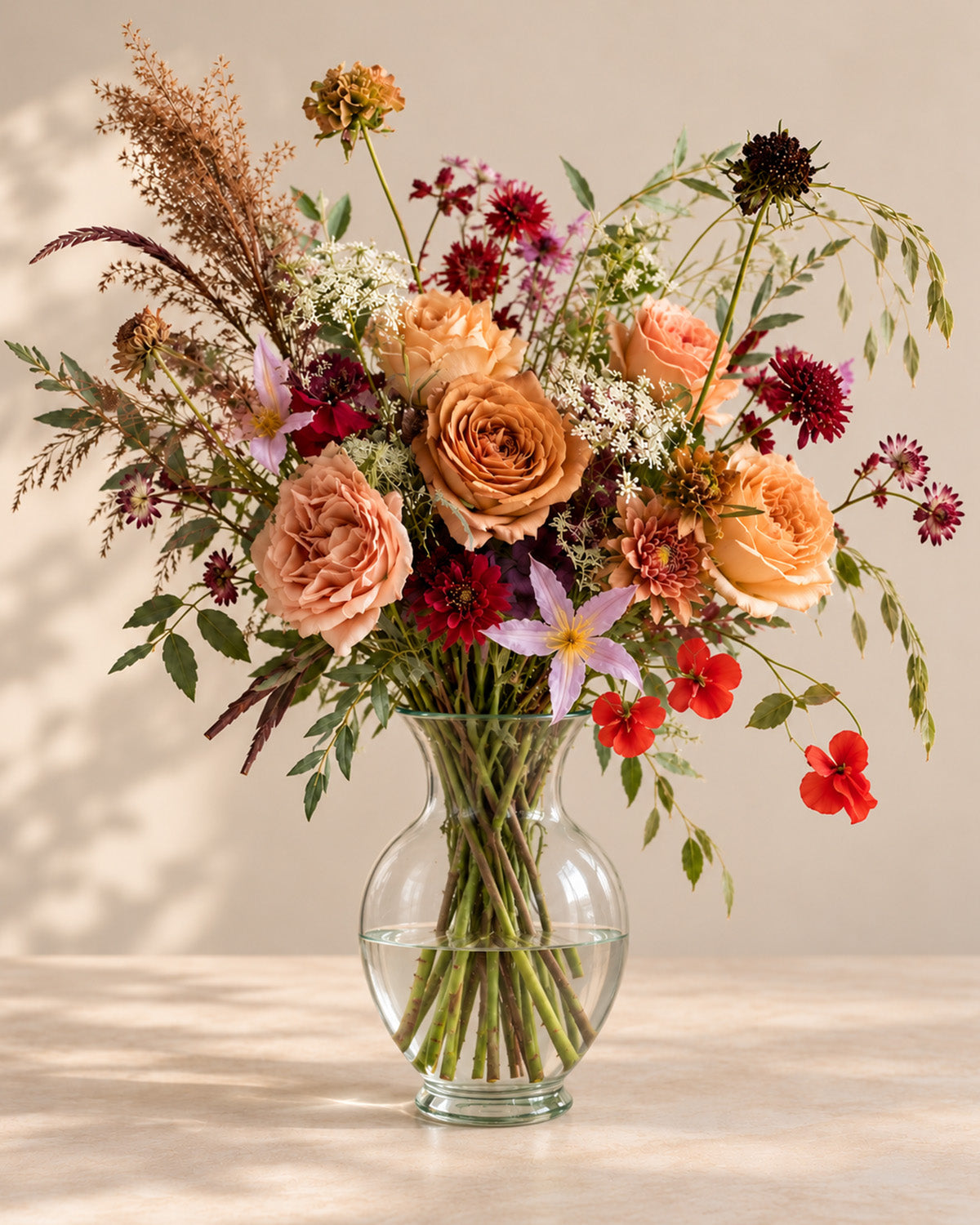 Vintage Ember bouquet with caramel roses, burgundy flowers, soft peach blooms and airy greenery in a clear glass vase