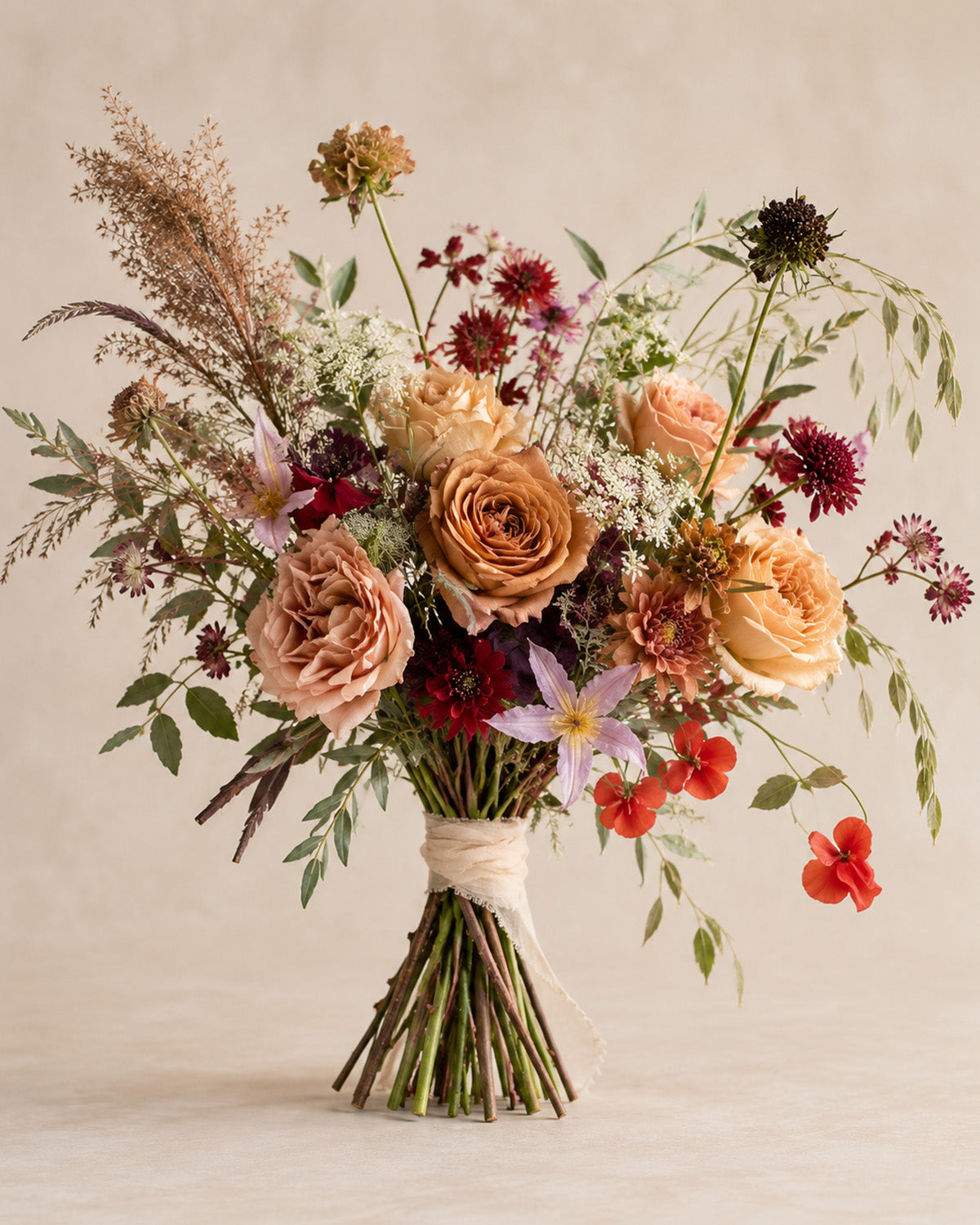 Vintage Ember bouquet hand-tied with caramel roses, burgundy flowers, soft peach blooms and airy greenery
